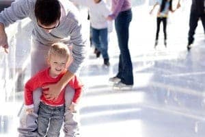A father and son going ice skating at a rink.